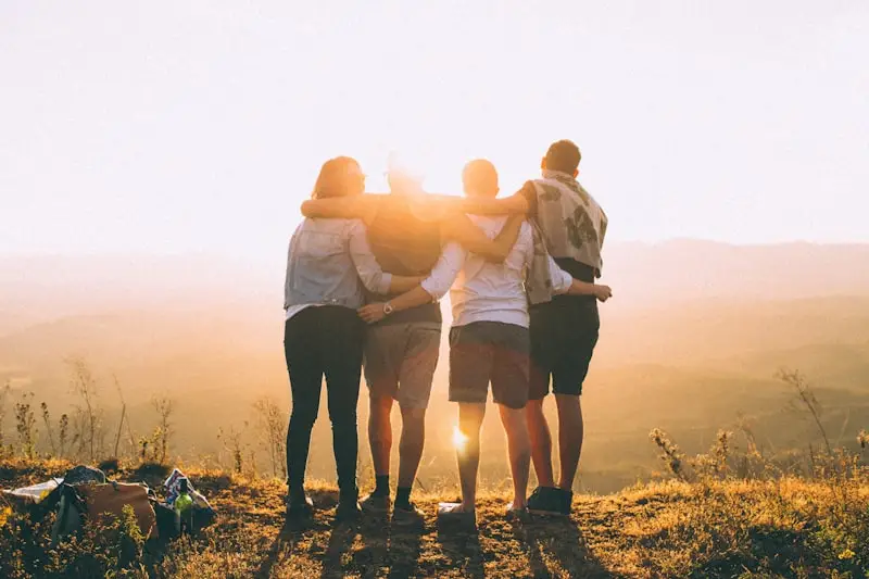 Grupo de adultos abrazados mirando el atardecer desde una colina