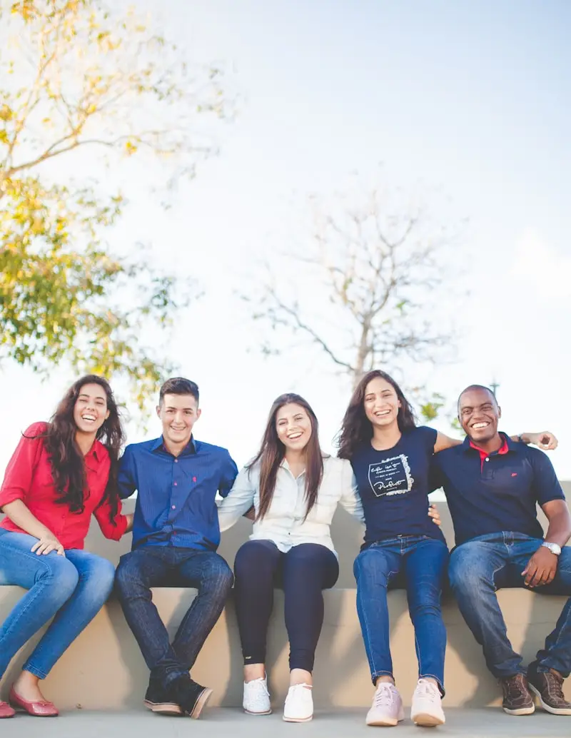 Grupo de jóvenes riendo sentados en un muro al aire libre